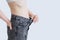 Caucasian woman in gray jeans pulls off the belt of trousers with her hand. Diet weight loss concept. White background