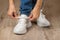 Caucasian woman hands tie elastic laces on chunky sole white sneakers shod on her feet on the brown floor. Pair of new comfortable