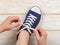 Caucasian woman hands tie white elastic laces on classic blue  gumshoes or sneakers indoor. Comfortable shoes for fitness and