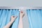 Caucasian woman hangs blue curtains on cornice close-up