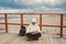 Caucasian woman in hat and jacket with backpack in winter sits on wooden pier on beach near North Sea. Denmark