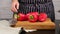 Caucasian woman in the kitchen piles whole red ripe peppers on brown kitchen board