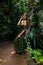 Caucasian woman leaning against a tree in tropical rain forest. Beautiful woman wearing long green dress. Walking trail in jungle