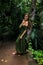 Caucasian woman leaning against a tree in tropical rain forest. Beautiful woman wearing long green dress. Walking trail in jungle