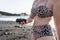 Caucasian woman in leopard bikini showing volcanic stone in black sand beach in the sunset. White woman holding wet lava rock in