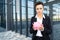 Caucasian woman in office clothes holds a pink pig moneybox and waits a coleague near the office building