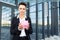 Caucasian woman in office clothes holds a pink pig moneybox and waits a coleague near the office building