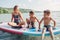 Caucasian woman parent sitting on paddle sup surfboard in water with kids children.