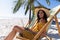 Caucasian woman sitting on a deck chair and using a laptop at the beach