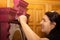 Caucasian woman with smile on face painting wooden ornamented cupboard in red with large paint brush with doors in