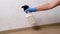 Caucasian woman sprays cleaner solution on wall to remove mold. Female hand in blue rubber glove uses cleaning product