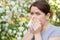 Caucasian woman suffers from allergies and sneezes while walking in the park.