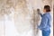 Caucasian woman tearing off old wallpaper from wall preparing for home redecoration