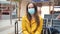 Caucasian woman tourist in waiting room with medical mask protection work in smartphone. Traveler woman in yellow with