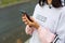 A Caucasian woman uses a smartphone via wired headphones with a headset. Phone in hand, white wire in ear, Enjoy label on hoodie.