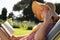 Caucasian woman wearing sunhat relaxing on sun lounger in sunny garden reading book