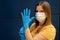 Caucasian woman wearing white disposal protective face mask putting on blue protective gloves. Corona virus pandemic