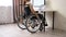 A Caucasian woman in a wheelchair drives up to her desk and starts typing with a laptop from home. Remote work for