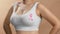 Caucasian woman in a white seamless bra and pink ribbon for breast cancer. Studio anonymous photo image on beige