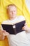 Caucasian young cool blond man in a white t-shirt is reading a book while lying down.