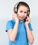 Caucasian young girl listening music with wireless headphones, blue t-shirt, grey background, looking at camera