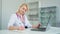 Caucasian young handsome physician sitting at table in cabinet and making notes in medical journal. The Female doctor