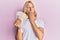 Caucasian young man with long hair holding 100 danish krone banknotes covering mouth with hand, shocked and afraid for mistake