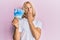 Caucasian young man with long hair holding 50000 indonesian rupiah covering mouth with hand, shocked and afraid for mistake