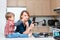 Caucasian young woman mother housewife taking pictures selfie in kitchen, her child son boy playing and drawing on her cheek