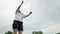 A Caucasian young woman playing at badminton. Slow motion. Bottom view, cloudy sky at the background. Sport and activity