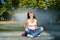 Caucasian young woman sitting by fountain enjoys coolness from water on sunny