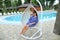 Caucasian young woman sitting in pendant white chair, swiming pool in background.