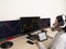 Caucasian young woman sitting at a table doing stock trading on a computer with three black monitors