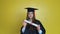 Caucasian young woman student shows her graduating diploma while staying in front of cameraon yellow background