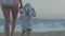 Caucasian young woman and two years old baby playing on sunset beach. Mother and daughter going to the waving sea.