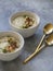 Cauliflower cream soup , decorated with fried cauliflower inflorescence in white bowls with golden spoons on a gray background
