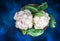 Cauliflower with leaves in a wooden bowl on a contrasting textured blue background