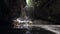 Cave waterfall in a rocky wall with water droping and flowing against sunlight.