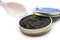 Caviar in a white nacre spoon with the metalllic box on white background