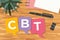 CBT (Cognitive Behavioral Therapy) written on colorful speech bubbles, flat lay desk view