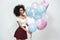 Celebrating birthday. Gorgeous afro american woman with curly hair holding colourful balloons while standing against