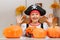 Celebrating Halloween at home. A cheerful little girl in a pirate costume sits at a table with pumpkins and a bucket