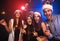 Celebrating New Year together. Group of beautiful young people in Santa hats throwing colorful confetti, looking happy