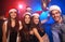 Celebrating New Year together. Group of beautiful young people in Santa hats throwing colorful confetti, looking happy