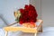 Celebrating Saint Valentine`s Day with bouquet of red roses and glass of champagne on tray on bed.