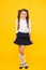 Celebrating September 1. Happy girl celebrating beginning of school year on yellow background. Small cute schoolchild in