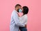 Celebrating Valentine`s Day during coronavirus epidemic. Black couple in face masks kissing on pink background