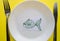 The celebration of April fool`s Day, a Plate with a fork and knife and a paper fish on a yellow colored background. Humor