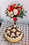 Celebratory homemade chokolate cake decorated with cream roses and red-white rose bouquet on table covered by macrame