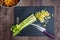 Celery stalks, with some chopped, on a black cutting board, chef knife, wood table, bowl of diced rainbow carrots